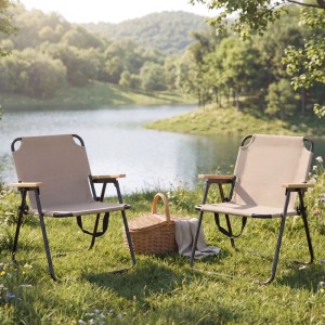Zwei cremefarbene Klapp-Campingstühle mit Bambus-Armlehnen und Metallgestell auf Gras am See, ideal für Outdoor.