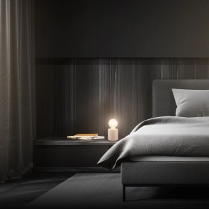 Beige Brilo Tischleuchte Tubo Keramik auf Nachttisch neben Bett.