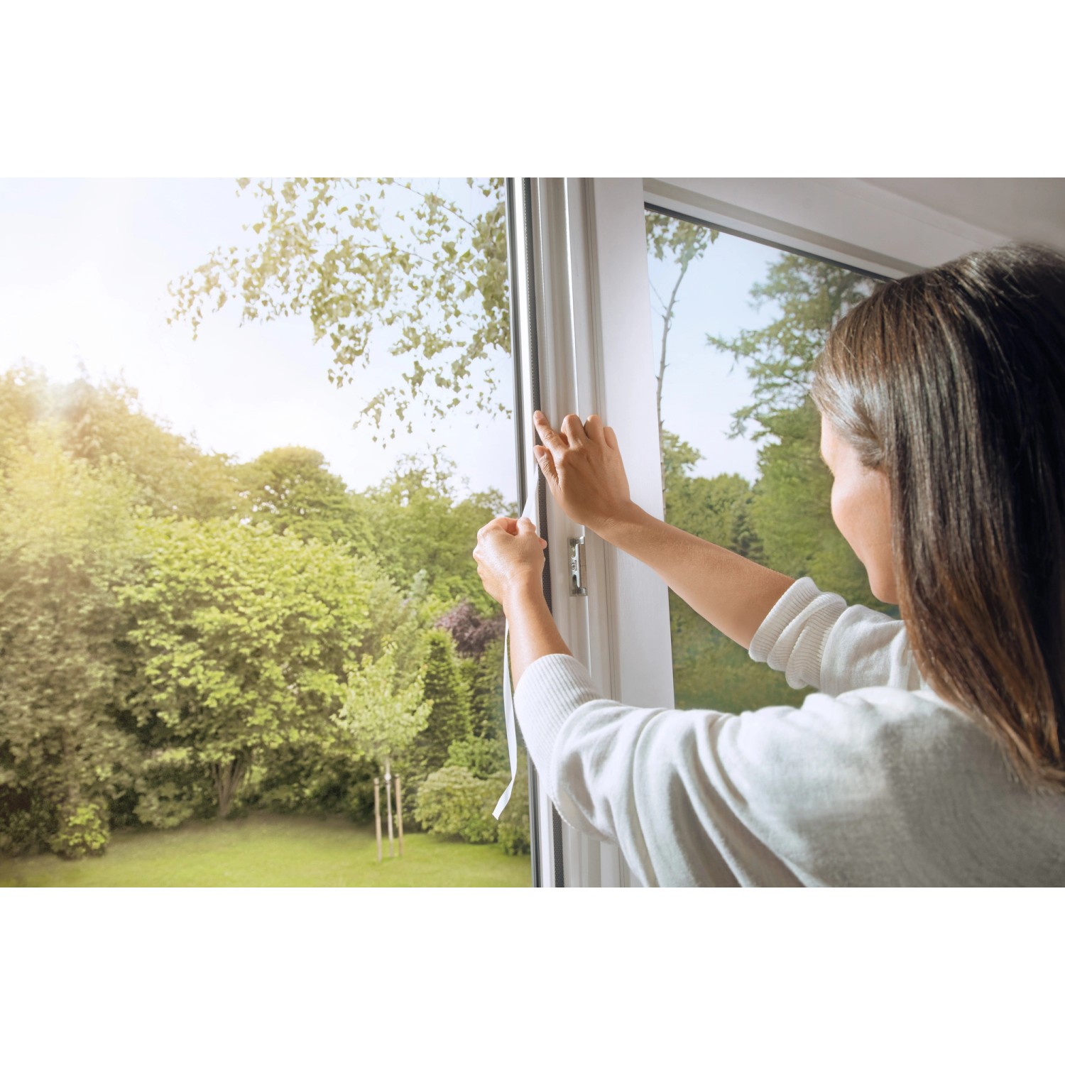 Frau montiert anthrazitfarbenes Tesa Pollenschutzgitter am Fenster.