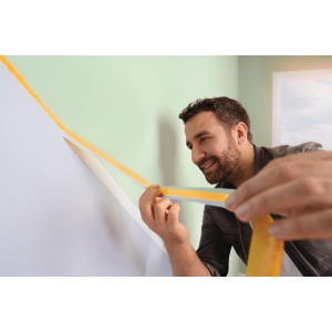 Mann klebt gelbes tesa® Malerband Perfect+ an eine Wand für scharfe Farbkanten.