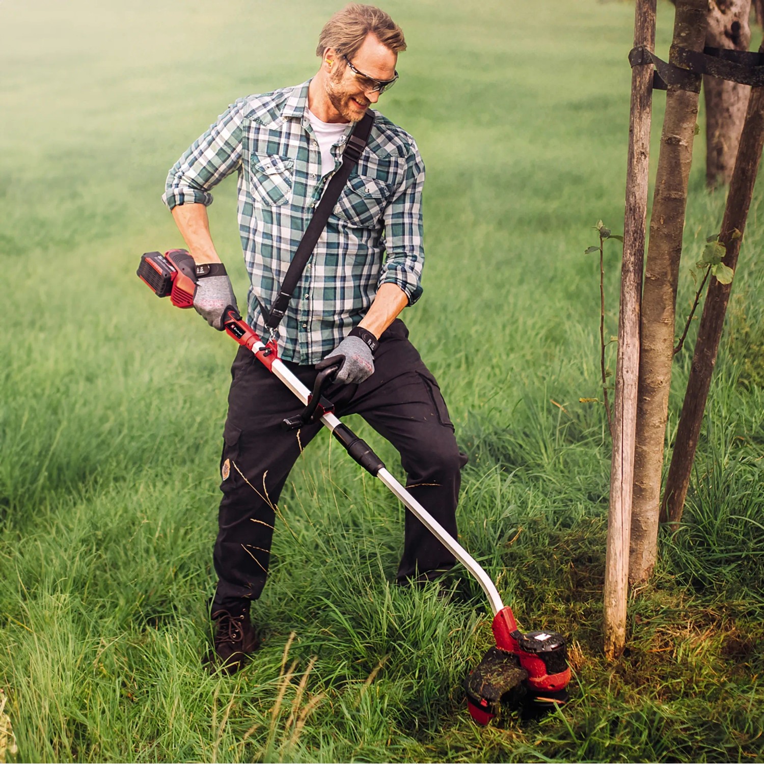 Mann trimmt Rasen mit Einhell Akku-Rasentrimmer GE-CT 36/30 Li E-Solo. Akku-Trimmer mit Tragegurt.