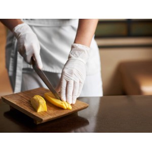 Szene: Person schneidet Mango mit weißen, latexfreien Einmalhandschuhen Gr. L auf Holzbrett.
