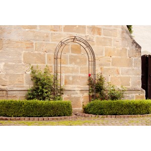 Eleo Rosenbogen Matera, pulverbeschichtet, 235x140x29,7 cm, vor Steinwand mit Rosen.