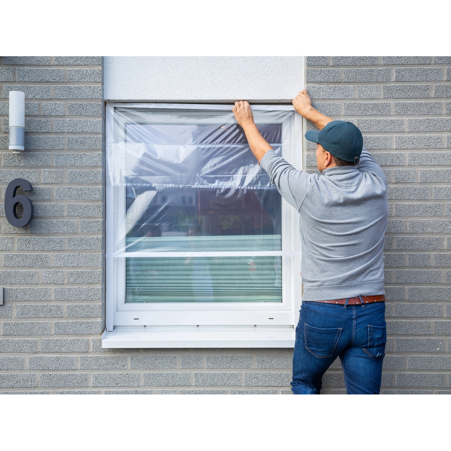 Mann befestigt transparente LUX Fensterschutzfolie am Fensterrahmen.