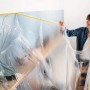 Frau bringt Tesa Abdeckfolie Easy Cover Perfect+ XL mit Klebeband an Wand an.