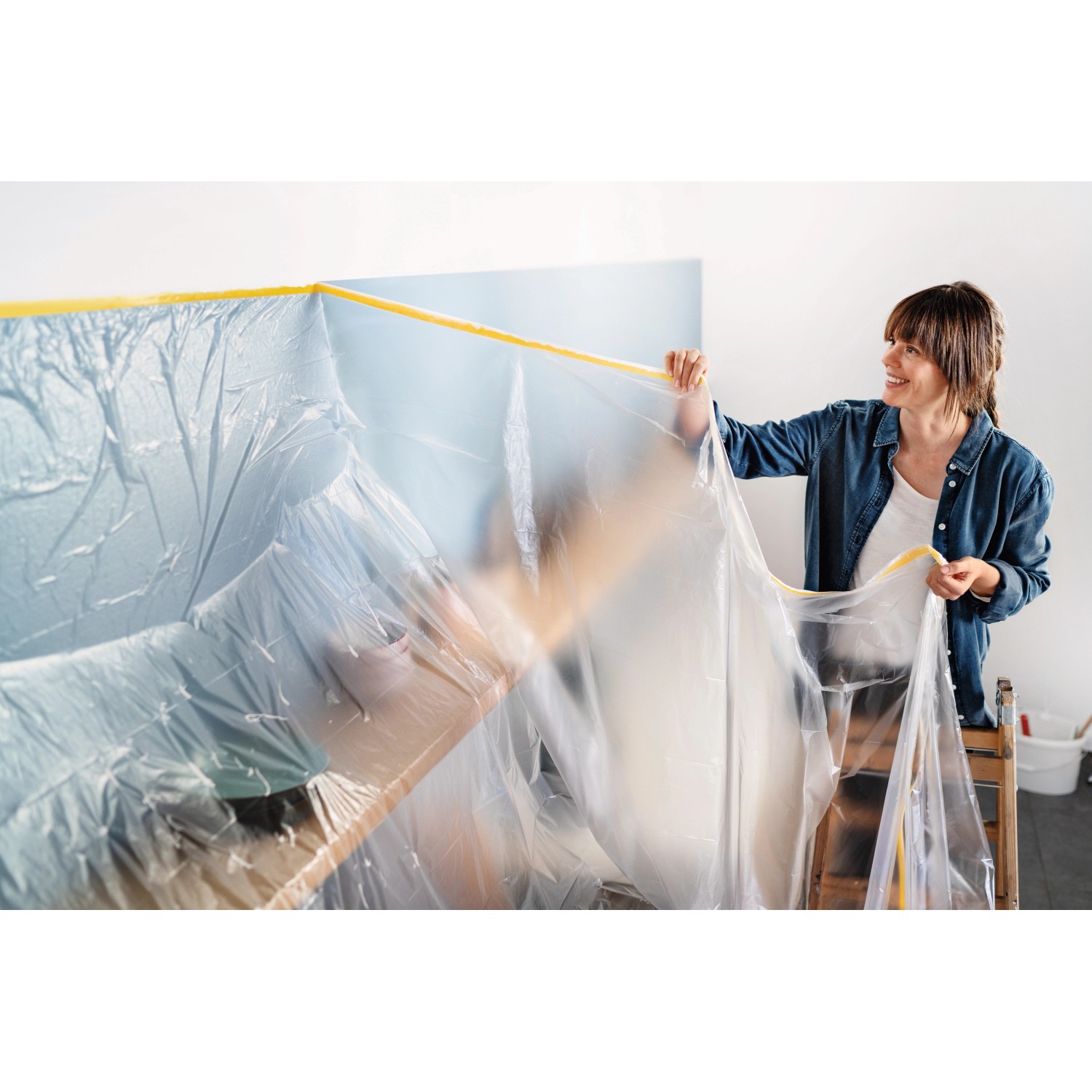 Frau bringt Tesa Abdeckfolie Easy Cover Perfect+ XL mit Klebeband an Wand an.