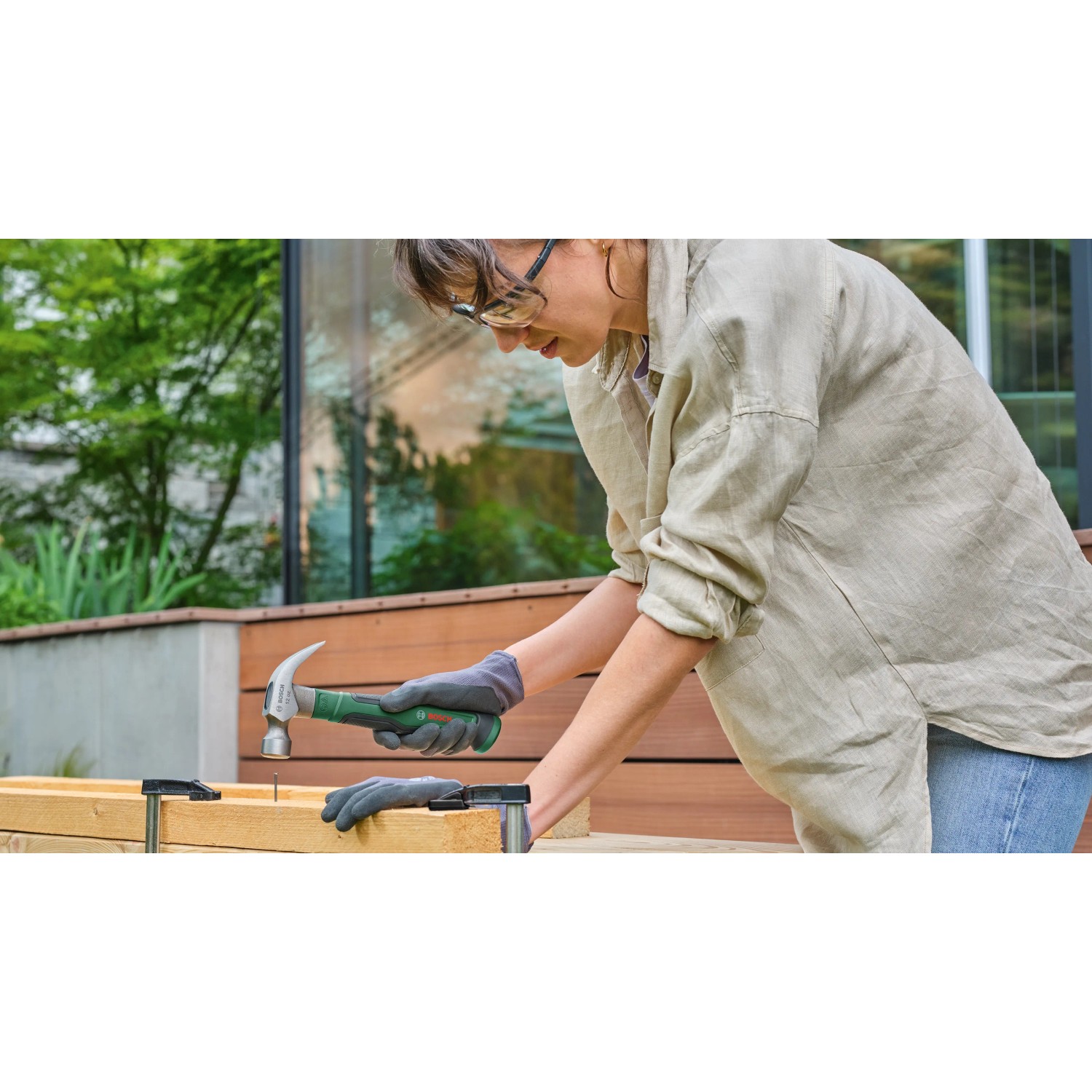 Frau arbeitet mit Hammer aus Bosch Werkzeugkoffer Advanced Set an Holzkonstruktion.