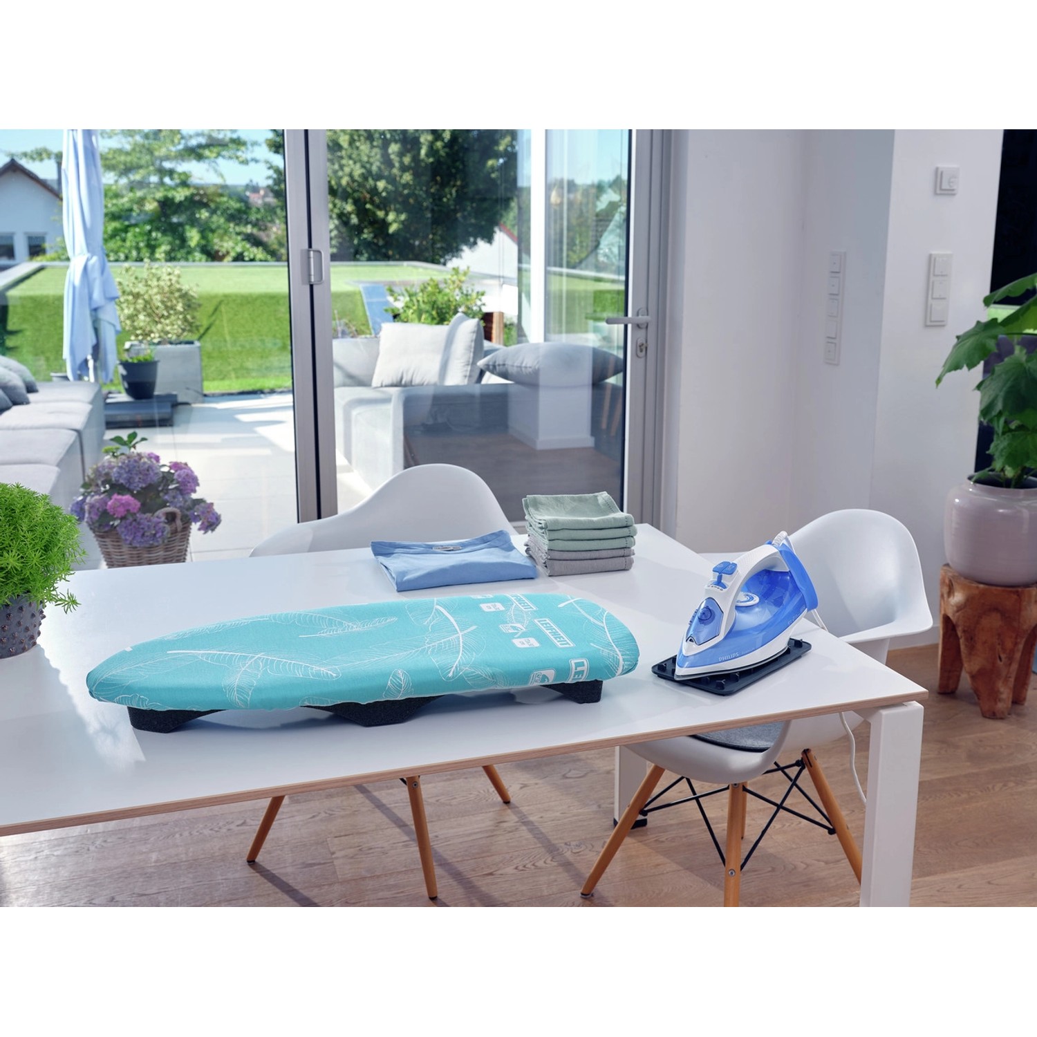 Leifheit AirBoard Compact Tischbügelbrett mit blauem Bezug und Bügeleisen auf einem Tisch.