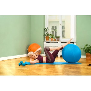Frau macht Crunches mit blauem Gymnastikball und orangefarbenem Sitting Ball Hocker im Hintergrund.