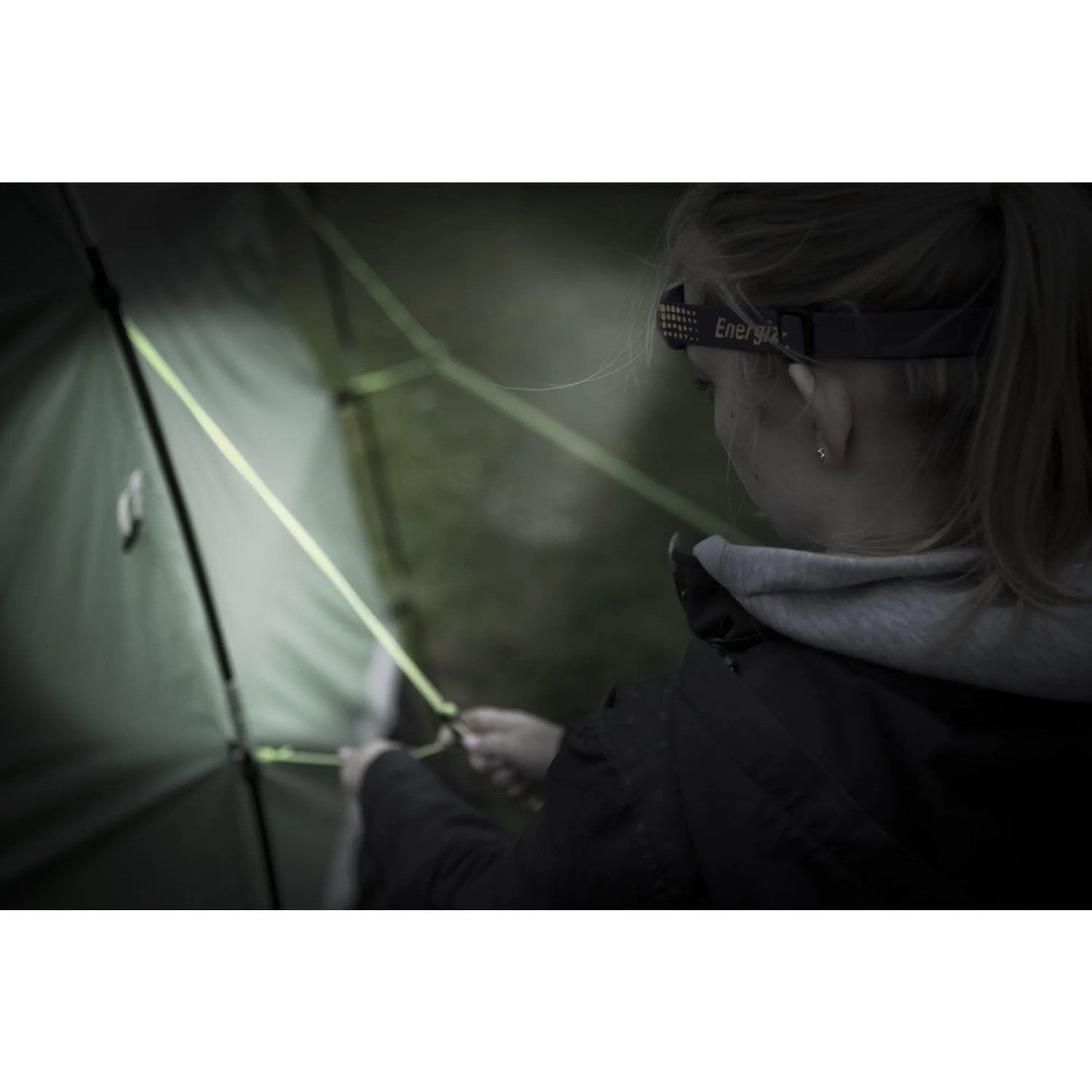 Frau beim Aufbau eines Zeltes mit Energizer Compact Sport Kopflampe. Taschenlampe leuchtet.