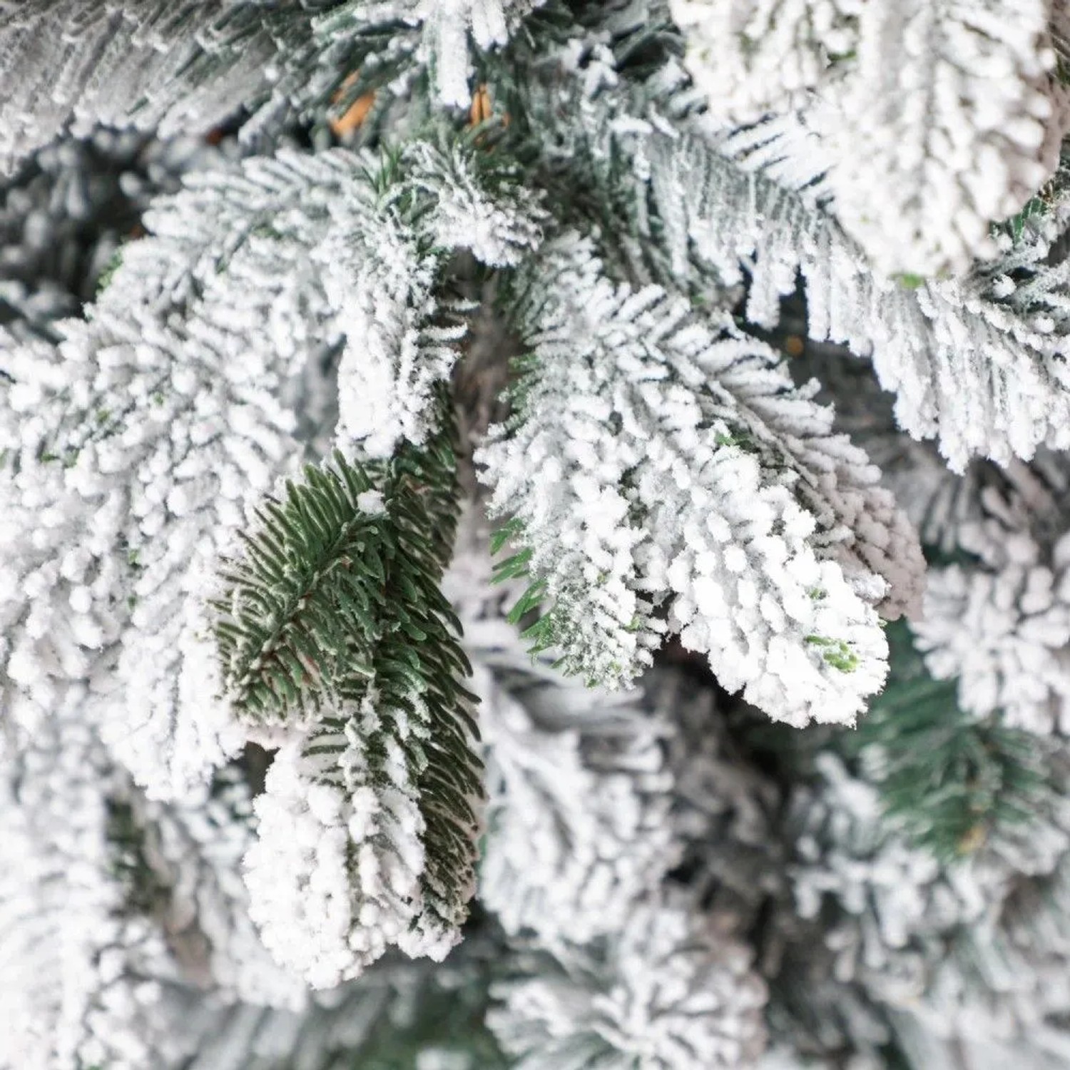 Detailaufnahme von einem künstlichen Weihnachtsbaum mit dichtem Kunstschnee auf grünen Zweigen. Perfekt für Weihnachtsdekoration.