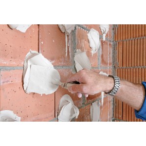 Anwendung von Knauf Perlfix Ansetzgips auf einer Ziegelwand mit einer Maurerkelle.