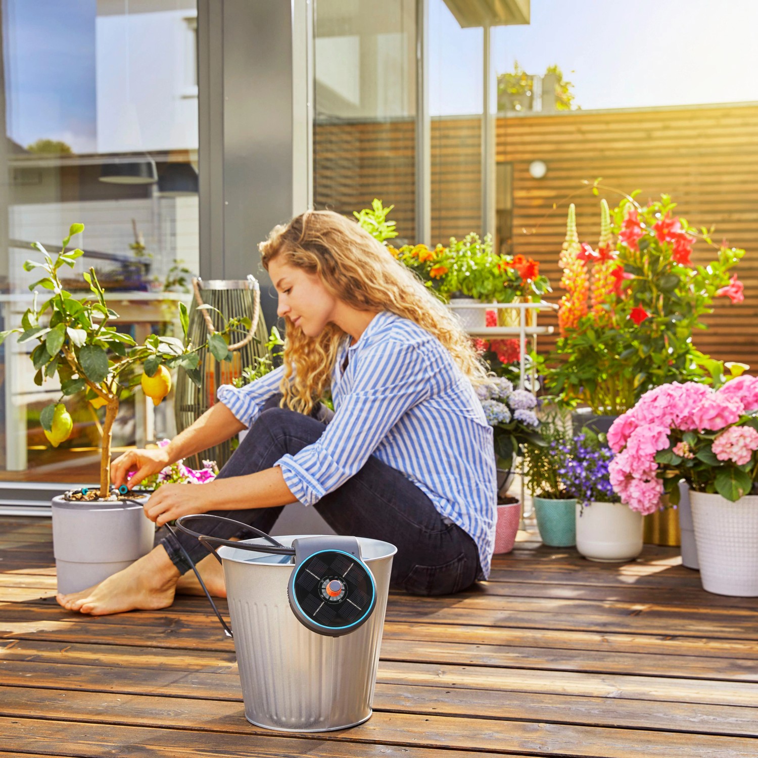 Frau bewässert Pflanzen mit Gardena Solar-Bewässerung Aqua Bloom Set auf Balkon/Terrasse.