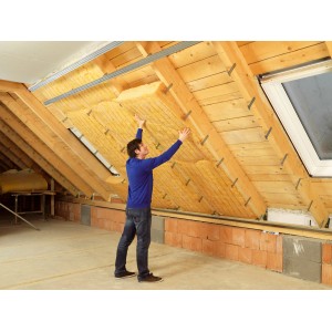 Ein Mann montiert Isover Uniroll Classic Klemmfilz (140mm) zur Zwischensparrendämmung im Dachausbau.