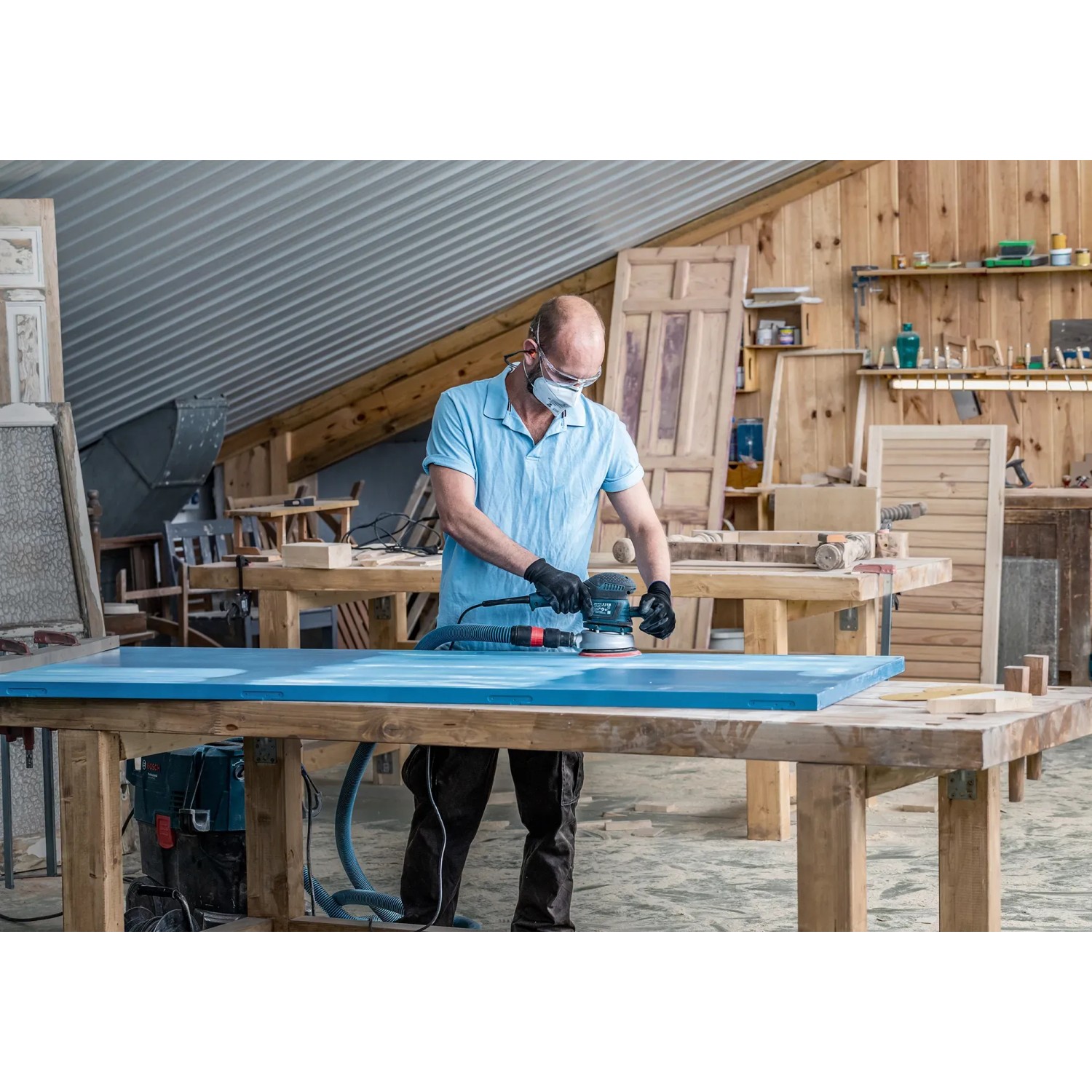 Handwerker schleift blaue Holzplatte mit Bosch Exzenterschleifer und Schleifblatt C470 K120.