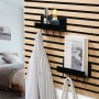 Schwarzes DenPanels Regal mit 4 Stiften an Akustikpaneel mit Deko und Jacke.