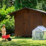 Vitavia Minigewächshaus Merlin neben Gartenhaus, Kind mit Schubkarre im Garten.