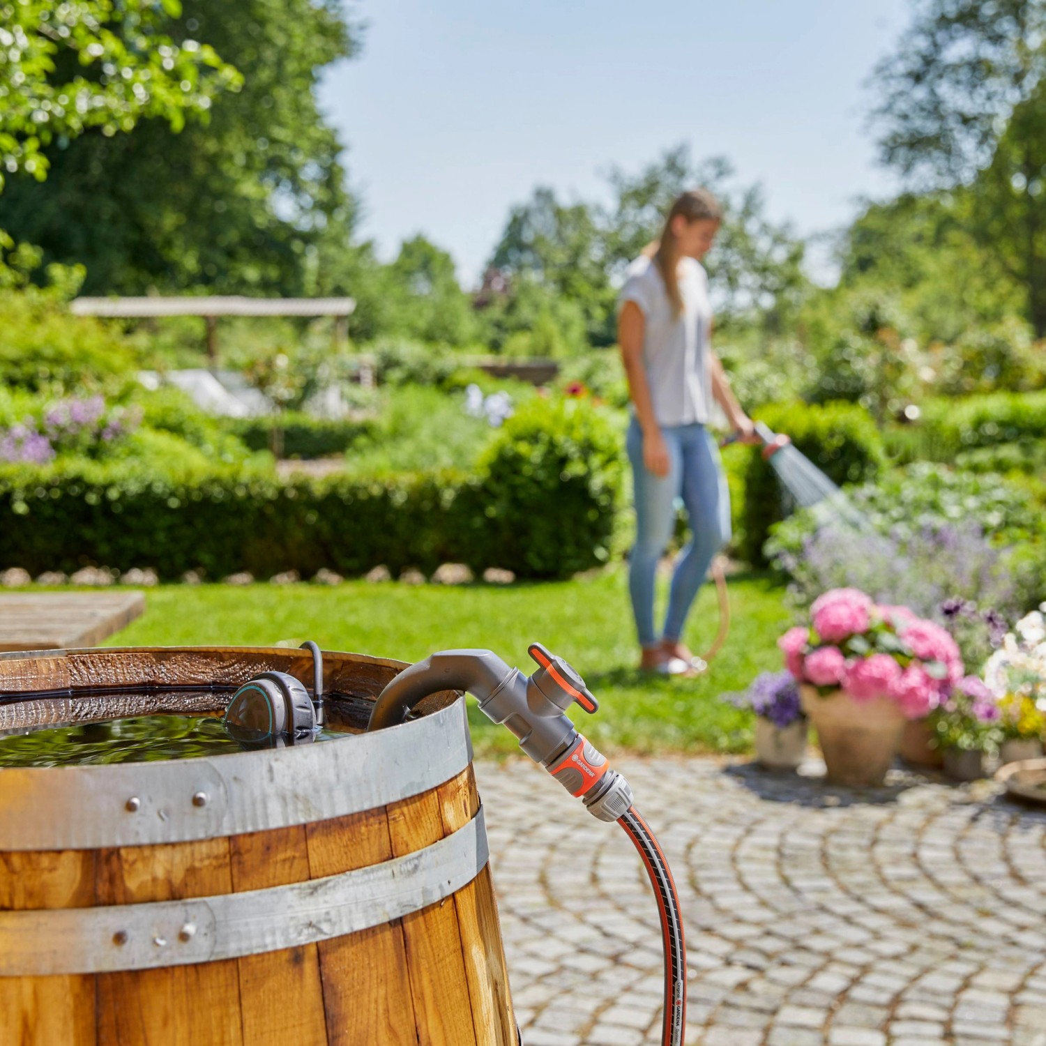 Gardena Regenfasspumpe 4000/1 im Einsatz: Frau bewässert Garten mit Regenwasser aus Holzfass.