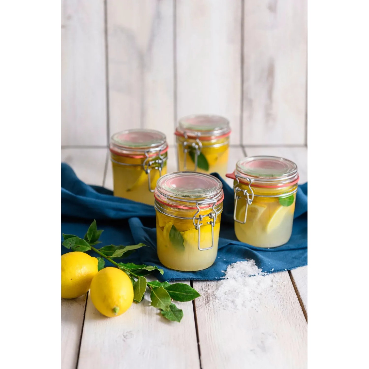 Dr. Oetker Bügelverschlussgläser (530 ml) gefüllt mit Zitronen und Kräutern auf blauem Tuch.