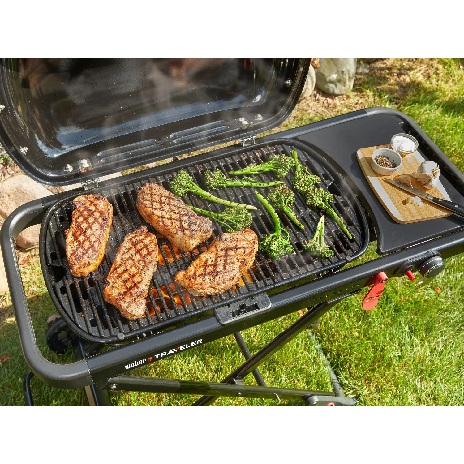 Weber Traveler Camping-Gasgrill mit Steaks und Brokkoli auf dem Grillrost.