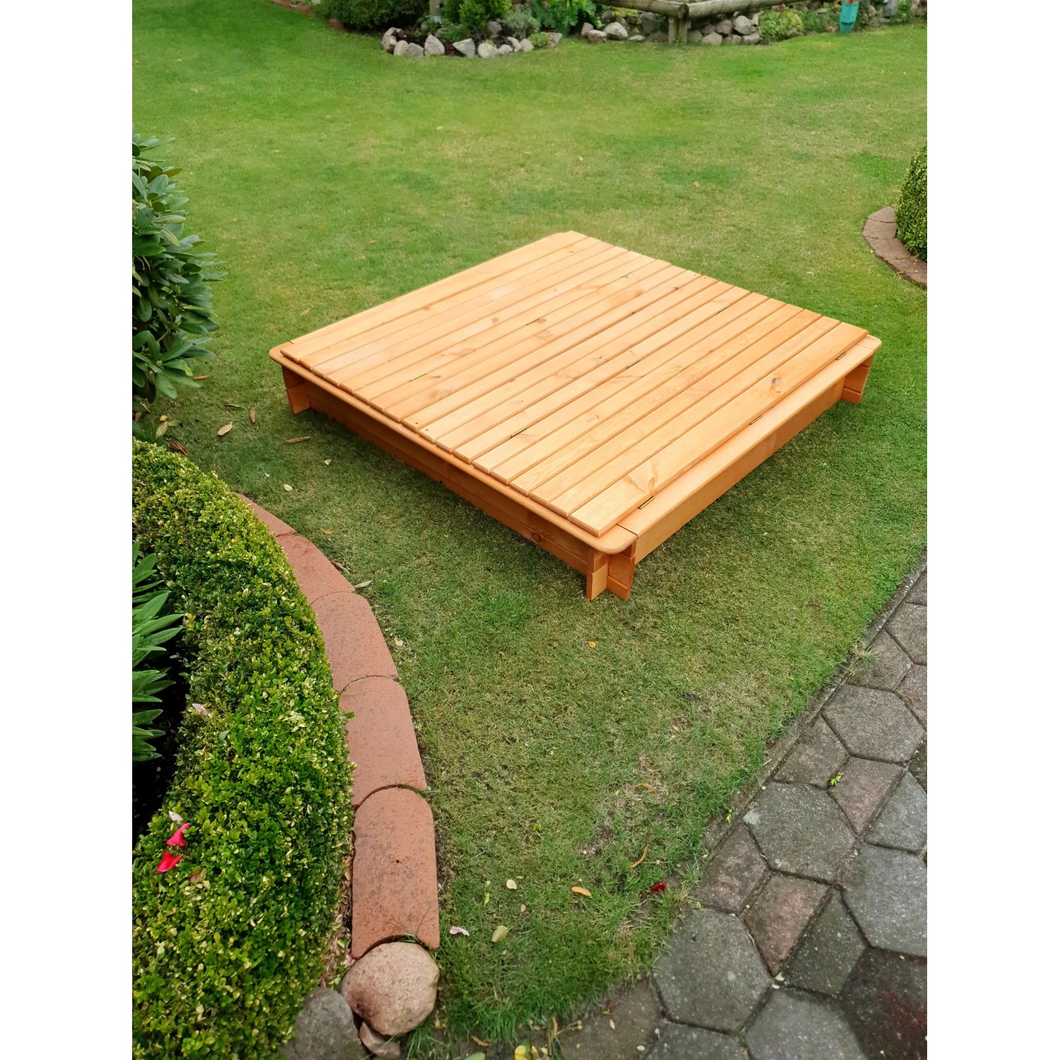 Quadratischer Sandkasten Donald 140x140 cm mit geschlossenem, klappbarem Holzdeckel im Garten.