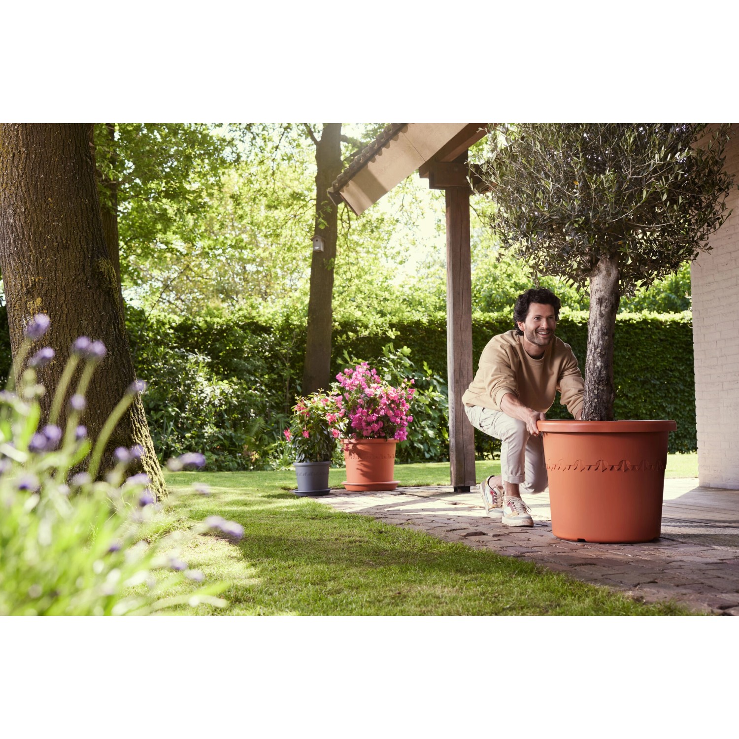 Elho Algarve Cilindro Blumentopf (Ø 48 cm) in Terrakotta mit Mann im Garten.