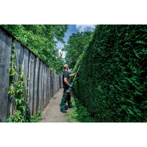 Mann schneidet hohe Hecke mit Metabo Heckenscheren-Aufsatz MA-HS 50. Akku-Heckenschere im Einsatz.