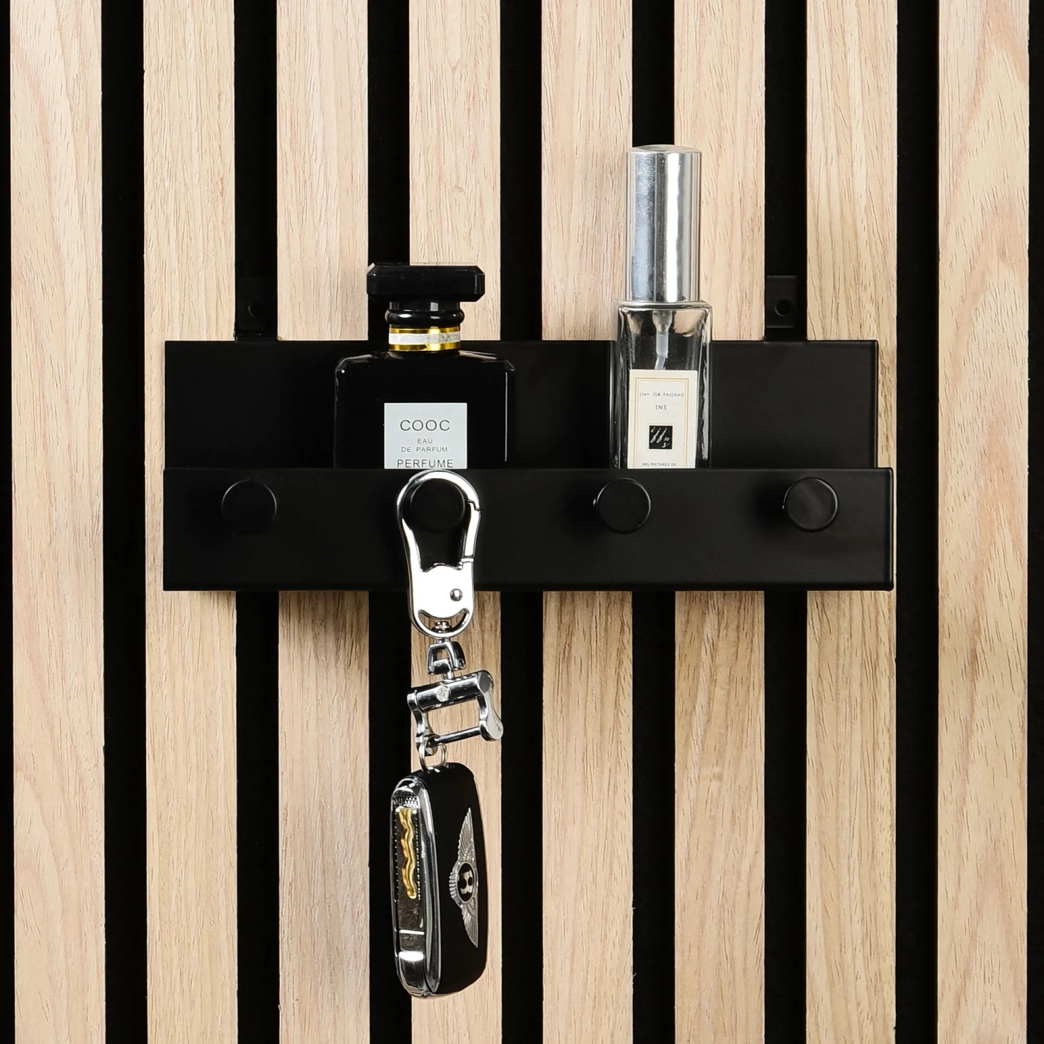 Schwarzes DenPanels Regal mit 4 Haken (21,5 cm) an Akustikpaneel mit Schlüssel und Parfümflaschen.