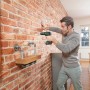Mann schraubt Regal mit Bosch Akkuschrauber UniversalImpact 18 an Backsteinwand.