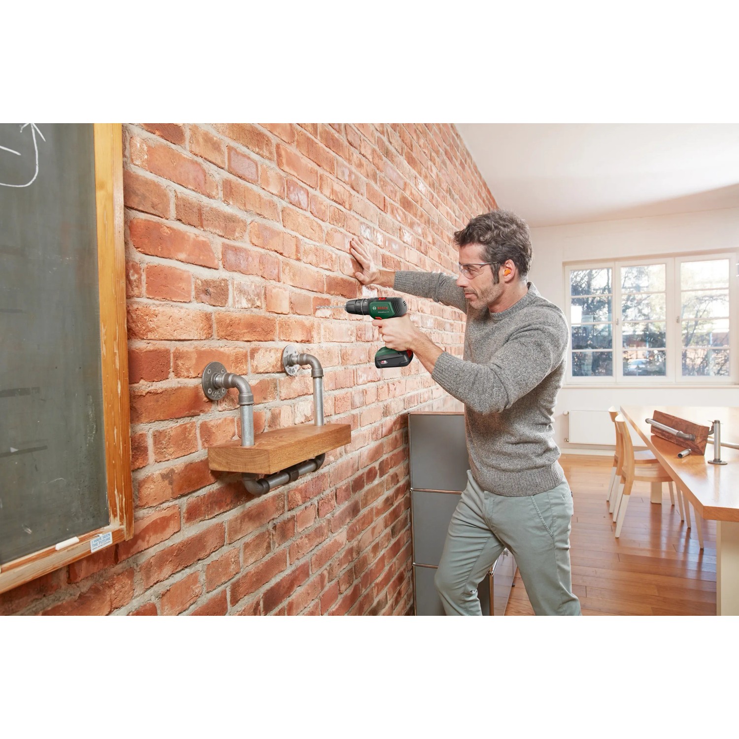 Mann schraubt Regal mit Bosch Akkuschrauber UniversalImpact 18 an Backsteinwand.
