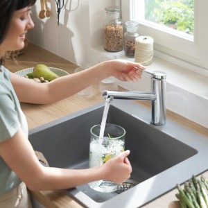 Frau befüllt Glas unter Hansgrohe Zesis Küchenarmatur M33 150 1jet in Chrom.
