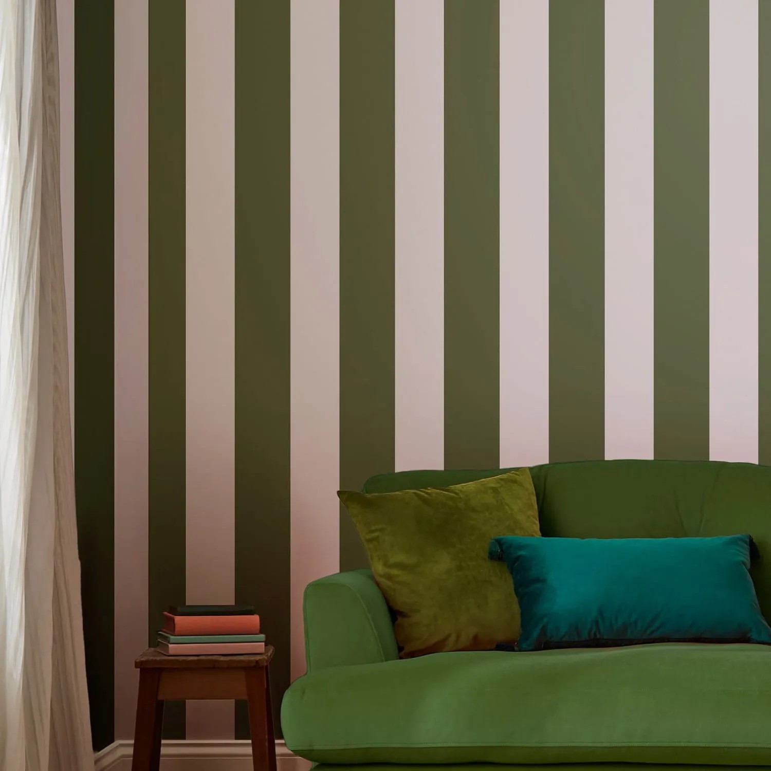 Joules Vliestapete Harborough Stripe Olive Green: Wand mit breiten, grünen und hellen Streifen hinter grünem Sofa.