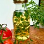 Bio-Majoran in Öl in Glasflasche, mit Tomaten und Majoranpflanze auf Holzbrett.