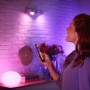 Frau steuert Philips Hue E27 LED Lampe mit Smartphone, farbige Beleuchtung im Raum.
