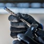 Bosch Expert Hammerbohrer SDS Plus-7X (13mm) im Bohrfutter, gehalten von Hand mit Arbeitshandschuh.