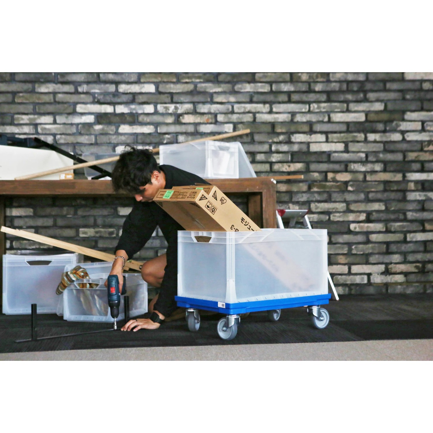 Blauer Eurobox-System Rollwagen 60x40 cm mit transparenter Box und Person bei Montagearbeiten.