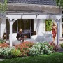 Freistehende, weiße Skan Holz Terrassenüberdachung Sanremo mit Polycarbonat-Dach und sitzenden Personen.