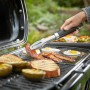 Weber Traveler Camping-Gasgrill in Aktion: Grillen von Speck, Eiern und Brot mit Grillzange.