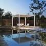 Elektrischer Weide Deluxe Plus Pavillon 4x4m, weiß, mit Lamellendach und LED-Beleuchtung auf Holzterrasse am Pool.