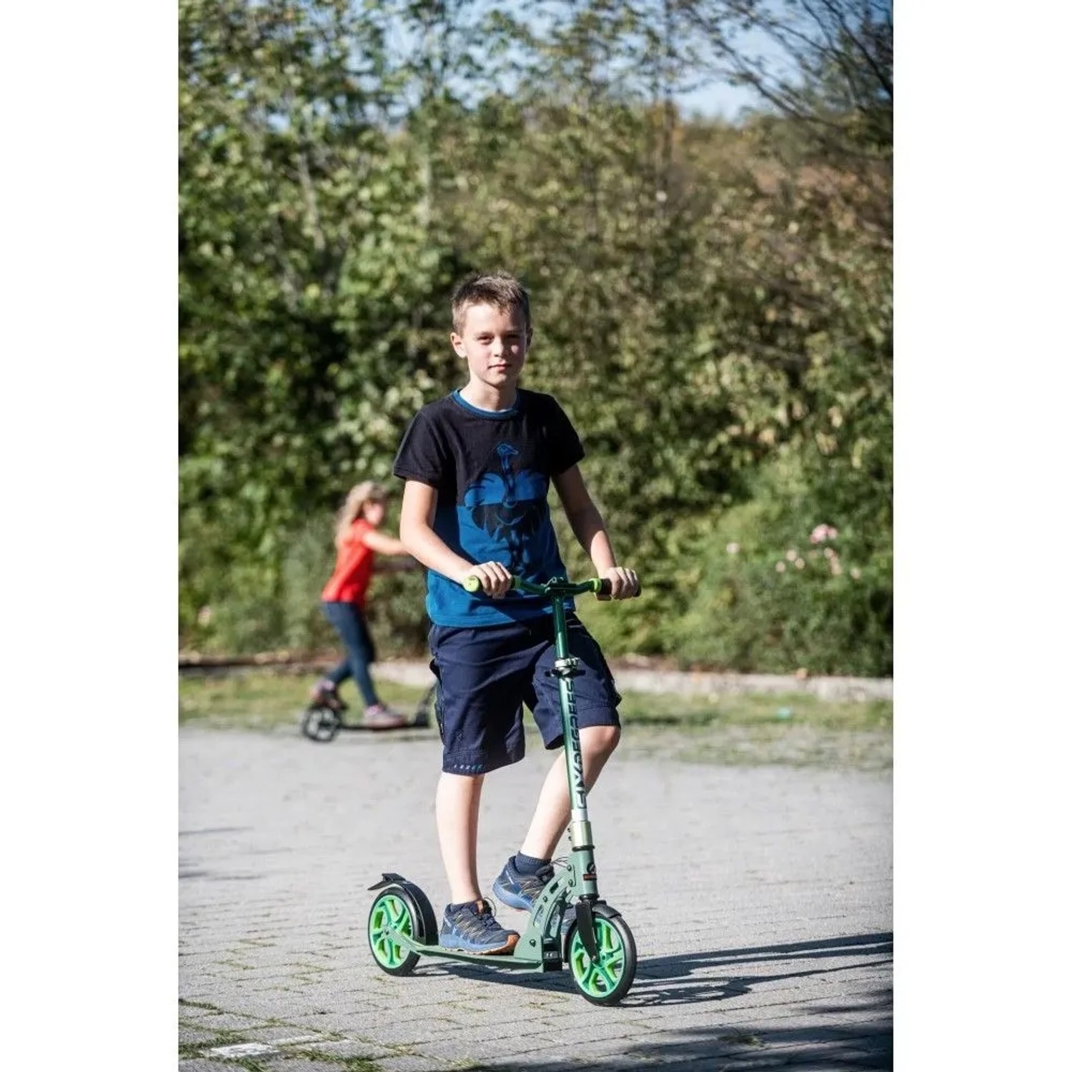 Junge fährt grünen Six Degrees Aluminium Scooter mit 205 mm Rollen und Klappmechanismus im Park.