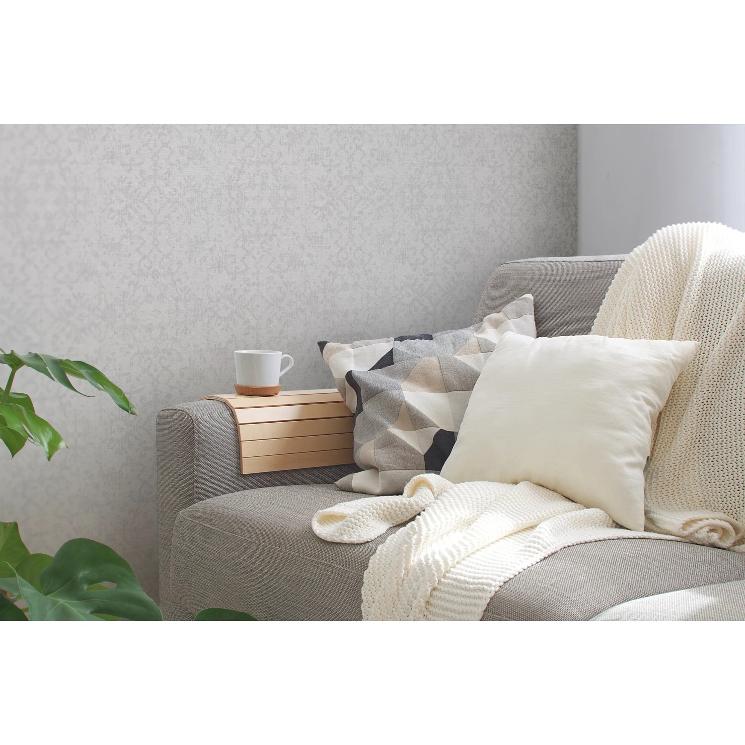 Helle, leicht strukturierte Ethno Vliestapete in Weiß und Grau an der Wand hinter einem Sofa.