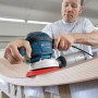 Mann schleift gebogenes Holz mit blauem Bosch Professional Exzenterschleifer GEX 40-150. Leistungsstarke Schleifmaschine.