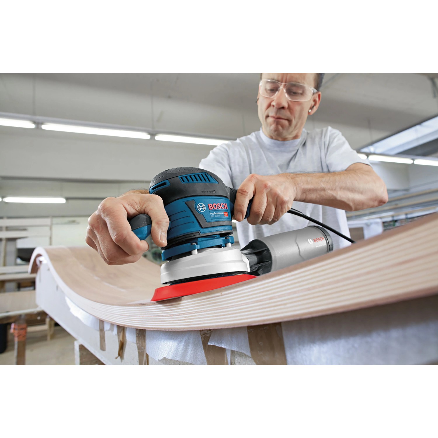Mann schleift gebogenes Holz mit blauem Bosch Professional Exzenterschleifer GEX 40-150. Leistungsstarke Schleifmaschine.