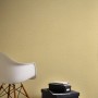 Gelbe, leicht strukturierte Vliestapete Uni Matt von OBI, gezeigt mit Stuhl und Deko.