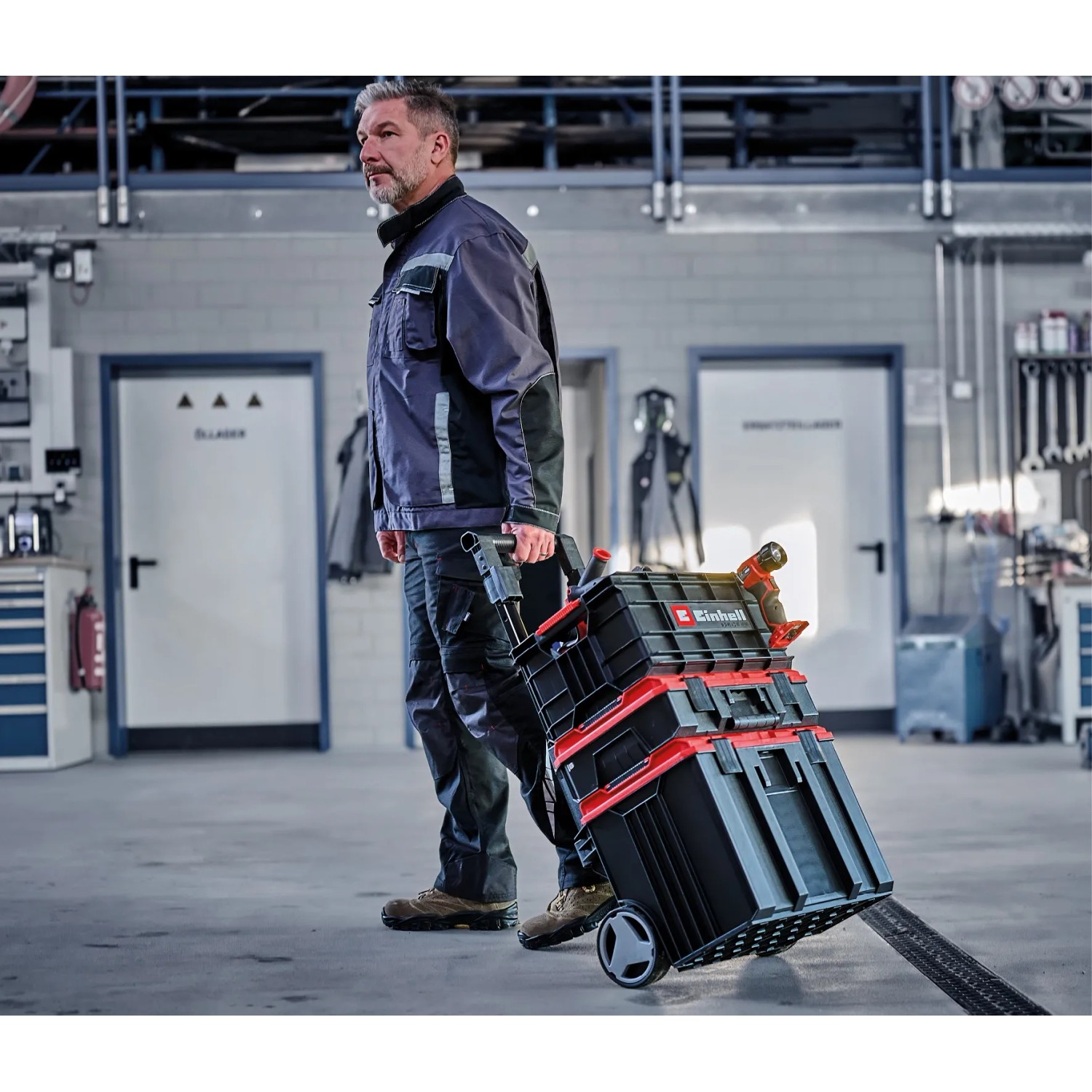 Ein Mann zieht einen Einhell E-Case Werkzeugkoffer Trolley mit Werkzeug in einer Werkstatt.