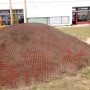 Rote Rasengitter-Fallschutzplatte 100x100 cm auf einem Hügel, geeignet für Spielplätze.
