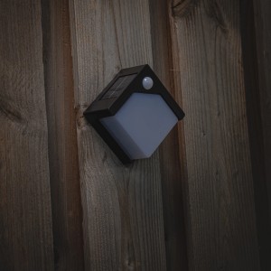 Schwarze Solar-Wandleuchte Pretoria mit Sensor an Holzwand. Außenleuchte mit Bewegungsmelder.