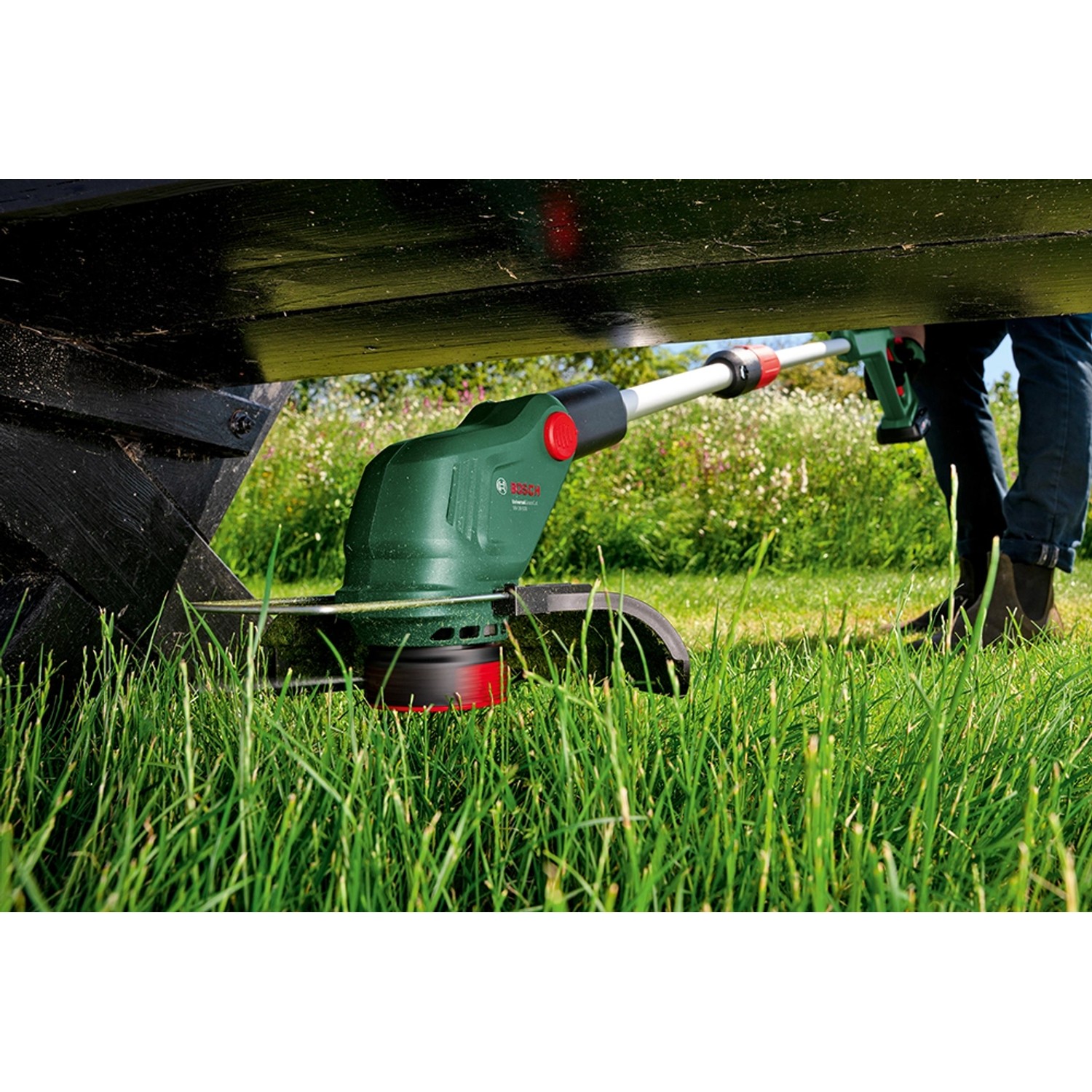 Bosch Akku-Rasentrimmer UniversalGrassCut 18V-26-500 beim Trimmen unter einer Bank.