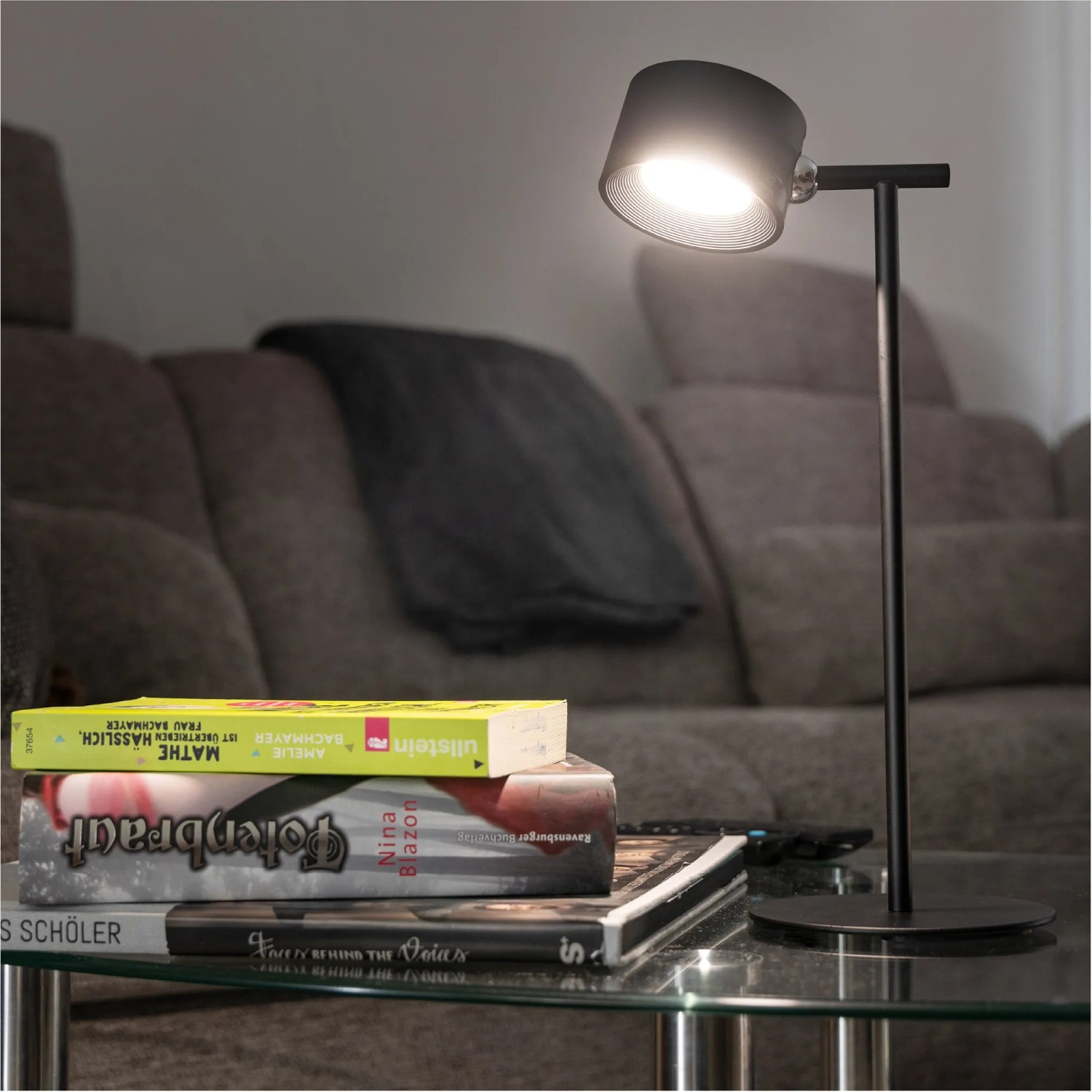 Schwarze LED Akku Tischlampe 3in1 auf einem Tisch mit Büchern, dimmbar und mit verschiedenen Lichtfarben.