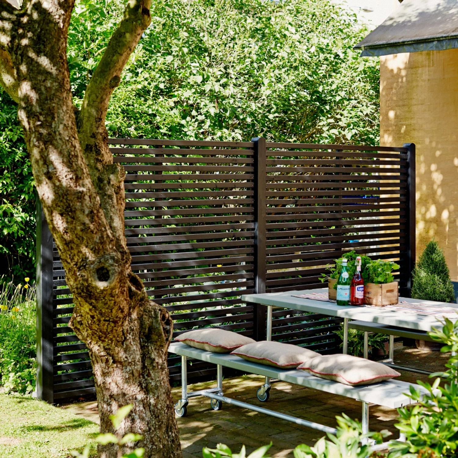 Schwarzer Sichtschutzzaun Tokyo aus Nadelholz, 180x180 cm, im Garten mit Tisch und Bank.